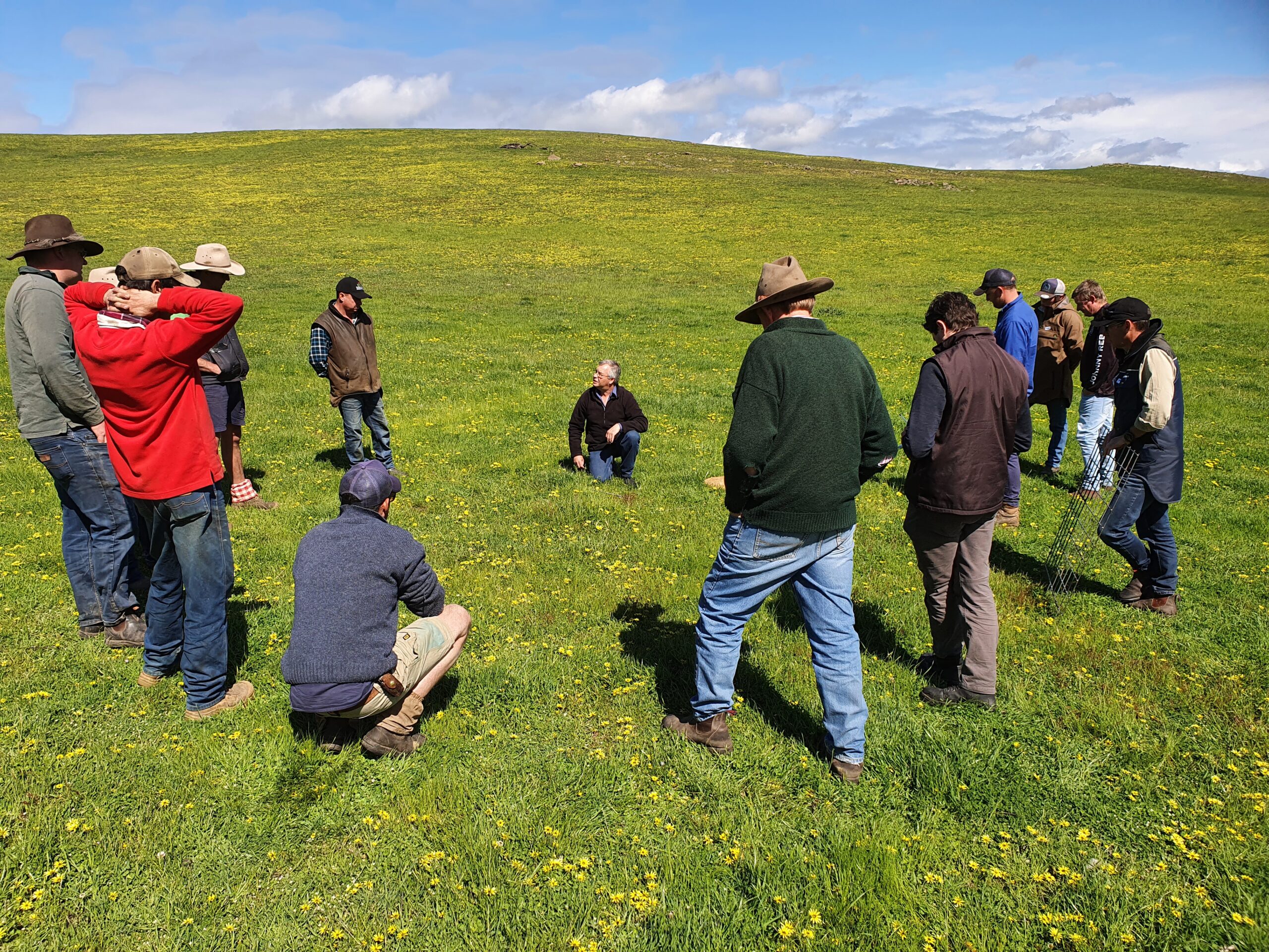 Group of people in a field standing in a circle and listening to a speaker